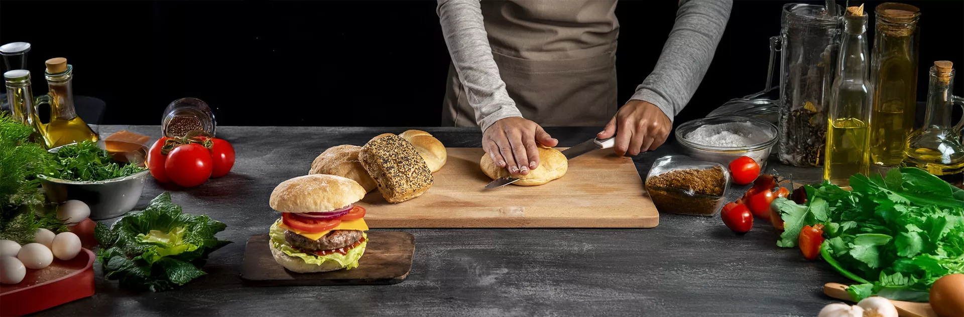 Pessoa cortando pão artesanal em bancada com hambúrguer montado, ingredientes frescos, temperos e azeites — mostrando o preparo rápido e personalizado de lanches com apoio do CNM para agilidade e controle no atendimento.